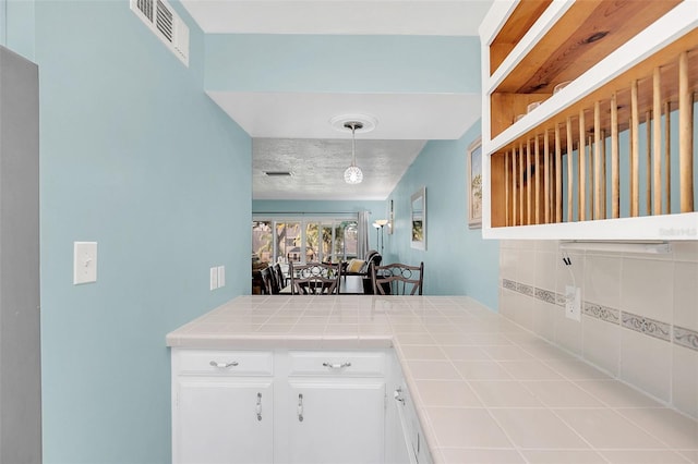 kitchen with pendant lighting, white cabinetry, backsplash, a textured ceiling, and tile countertops