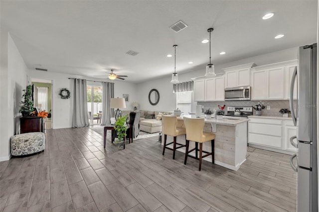 kitchen with white cabinetry, hanging light fixtures, appliances with stainless steel finishes, a kitchen island with sink, and decorative backsplash