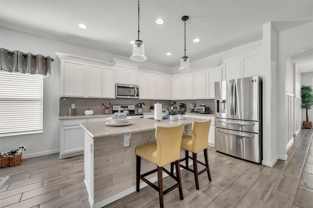 kitchen with stainless steel appliances, a kitchen island with sink, pendant lighting, and white cabinets