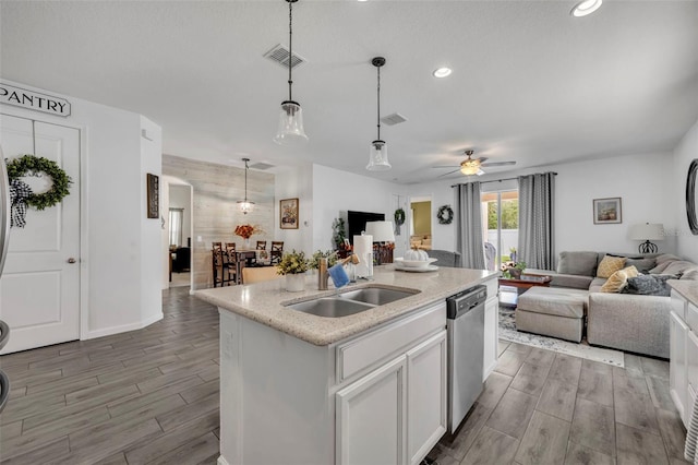 kitchen featuring dishwasher, sink, white cabinets, hanging light fixtures, and a center island with sink