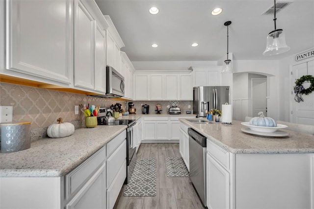 kitchen with appliances with stainless steel finishes, pendant lighting, white cabinetry, light stone countertops, and a center island with sink