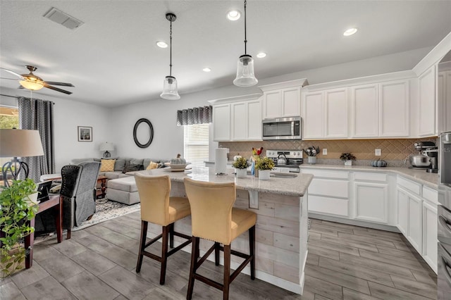 kitchen with a kitchen island, appliances with stainless steel finishes, pendant lighting, and white cabinets