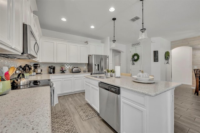 kitchen featuring appliances with stainless steel finishes, decorative light fixtures, white cabinets, decorative backsplash, and a center island with sink