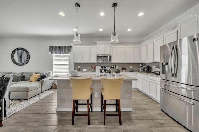 kitchen with pendant lighting, stainless steel appliances, white cabinets, and a center island with sink