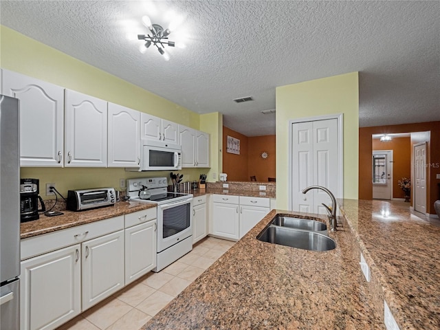 kitchen with a textured ceiling, white appliances, a sink, visible vents, and white cabinetry