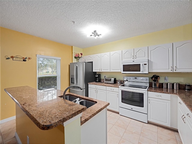 kitchen with a textured ceiling, a sink, light tile patterned floors, white cabinets, and white appliances