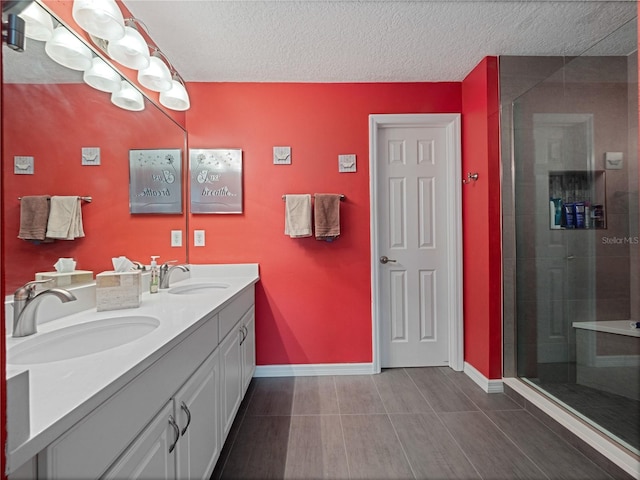 full bath featuring a sink, a textured ceiling, a stall shower, and double vanity