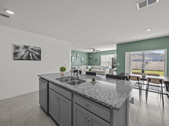 kitchen with sink, gray cabinets, dishwasher, a kitchen island with sink, and dark stone countertops