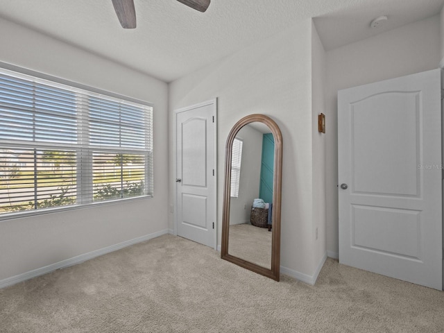 unfurnished bedroom featuring ceiling fan, light colored carpet, and a textured ceiling