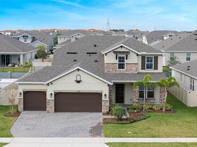 traditional home with fence, a shingled roof, a front lawn, stone siding, and decorative driveway