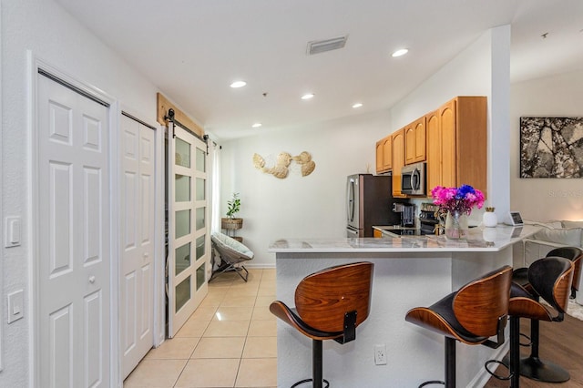 kitchen featuring light tile patterned floors, a kitchen breakfast bar, stainless steel appliances, kitchen peninsula, and a barn door