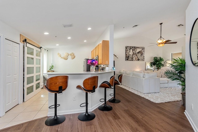 kitchen with a breakfast bar area, light hardwood / wood-style floors, kitchen peninsula, a barn door, and light brown cabinets