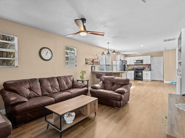 living room featuring a textured ceiling, light hardwood / wood-style floors, and ceiling fan