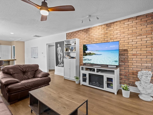 living room featuring ceiling fan, wood-type flooring, a textured ceiling, and brick wall