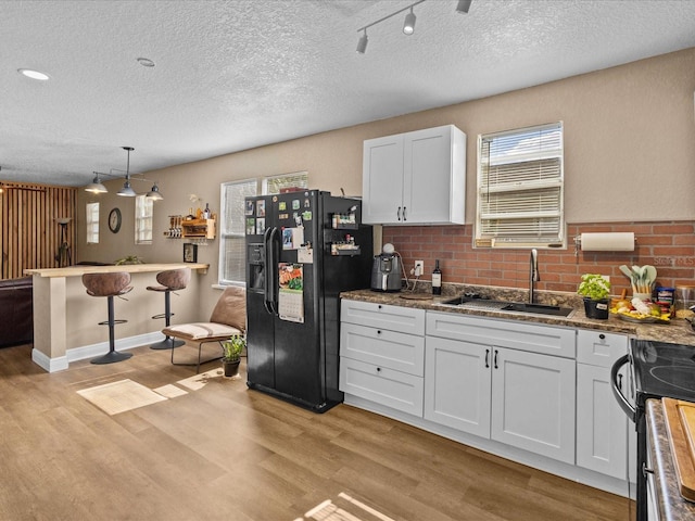 kitchen with pendant lighting, white cabinetry, sink, black fridge with ice dispenser, and light hardwood / wood-style floors