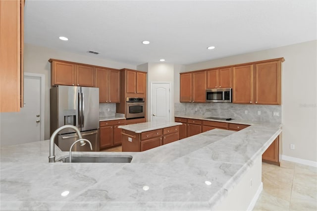 kitchen with stainless steel appliances, light stone countertops, sink, and a kitchen island