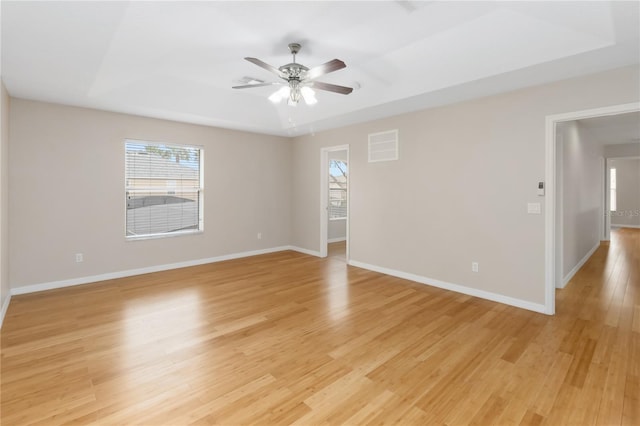 empty room with light hardwood / wood-style floors, a raised ceiling, and ceiling fan