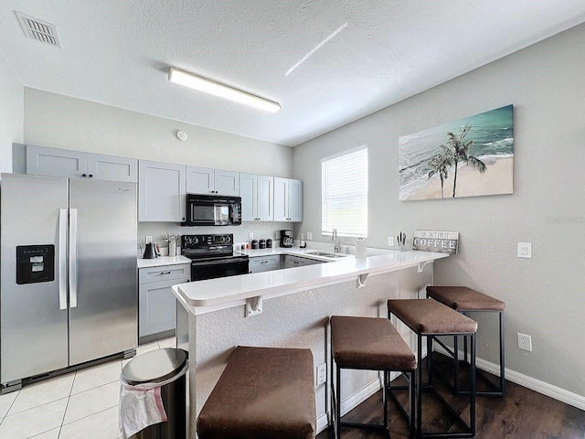 kitchen featuring sink, gray cabinets, a breakfast bar, black appliances, and kitchen peninsula