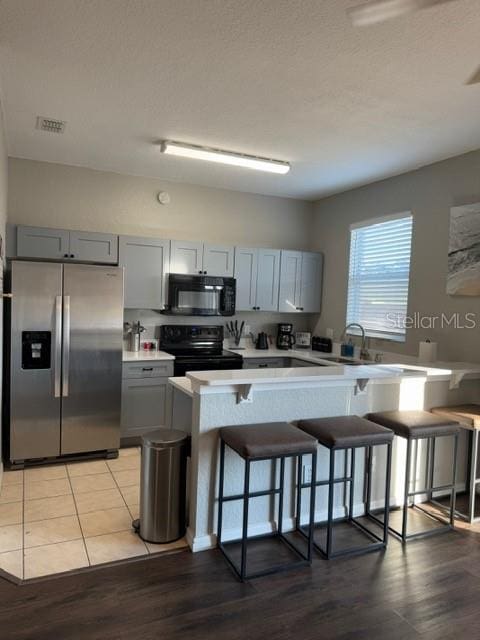 kitchen with black appliances, gray cabinetry, a sink, a breakfast bar area, and light countertops