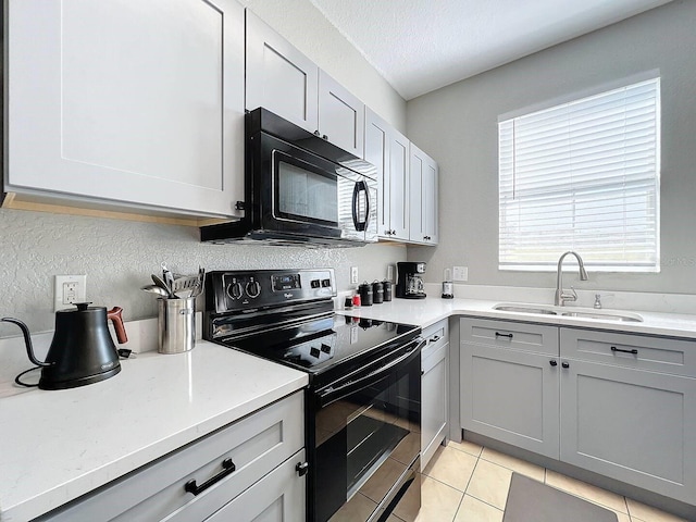 kitchen with sink, a textured ceiling, light tile patterned floors, light stone countertops, and black appliances