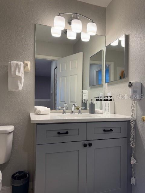 bathroom featuring toilet, vanity, and a textured wall