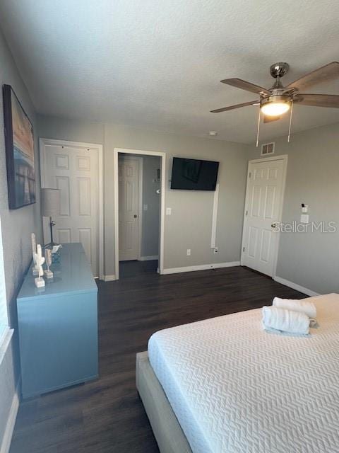 bedroom featuring ceiling fan, dark hardwood / wood-style floors, a textured ceiling, and two closets