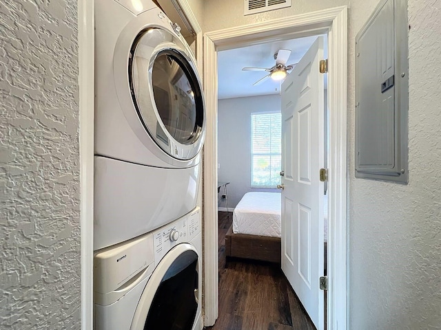 laundry area featuring stacked washer / dryer, ceiling fan, electric panel, and dark hardwood / wood-style flooring