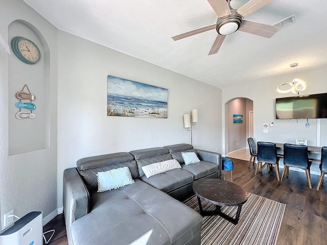 living room featuring dark wood-style floors, visible vents, baseboards, arched walkways, and ceiling fan