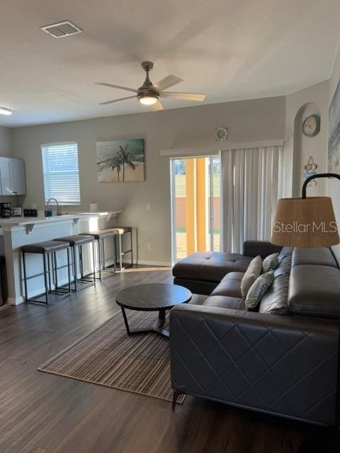 living room with visible vents, baseboards, dark wood-type flooring, and a ceiling fan