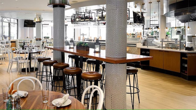 bar with light wood-style floors, ornate columns, and stainless steel gas cooktop