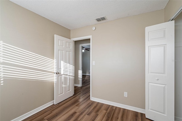 empty room with visible vents, a textured ceiling, baseboards, and dark wood-style flooring