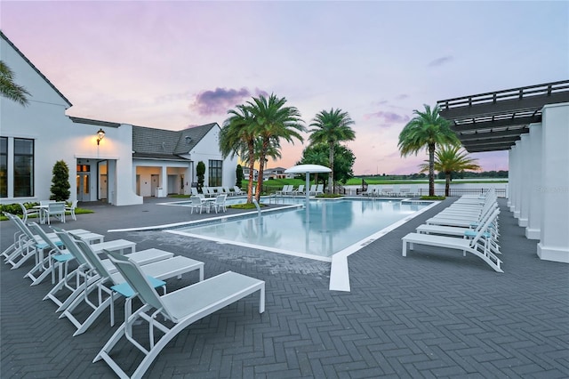 pool at dusk with a patio and a pergola