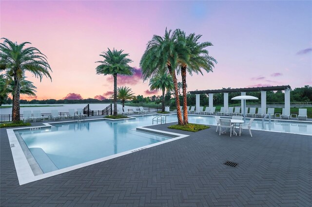 pool at dusk with a patio and a water view