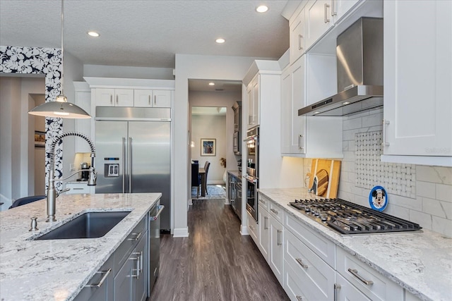 kitchen featuring white cabinetry, sink, wall chimney range hood, and decorative light fixtures