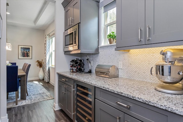 kitchen featuring stainless steel microwave, beverage cooler, backsplash, light stone countertops, and dark wood-type flooring