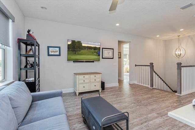 living room with ceiling fan with notable chandelier, light hardwood / wood-style floors, and a textured ceiling