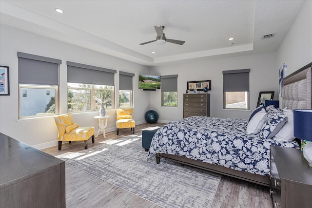 bedroom with a tray ceiling, wood-type flooring, a textured ceiling, and ceiling fan