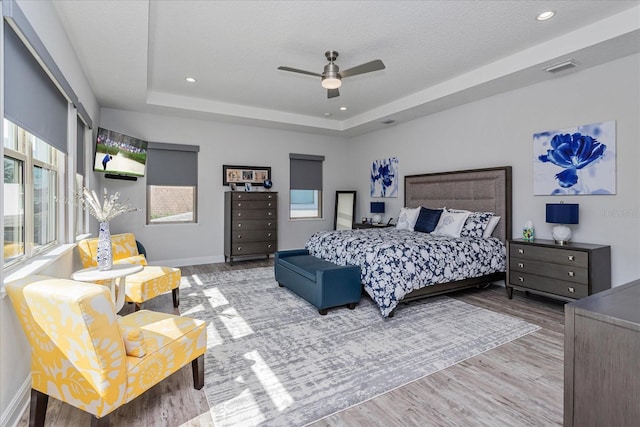 bedroom featuring hardwood / wood-style flooring, ceiling fan, a tray ceiling, and a textured ceiling