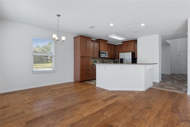 kitchen with stainless steel appliances, tasteful backsplash, wood-type flooring, a kitchen bar, and a chandelier