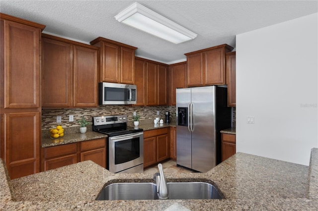 kitchen featuring tasteful backsplash, light stone countertops, appliances with stainless steel finishes, and sink