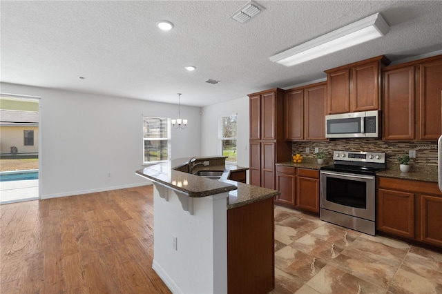 kitchen with appliances with stainless steel finishes, pendant lighting, sink, decorative backsplash, and a center island with sink