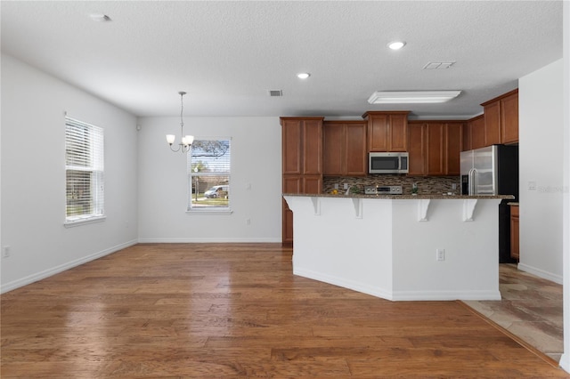 kitchen with pendant lighting, a kitchen bar, a center island with sink, and appliances with stainless steel finishes