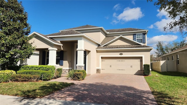 view of front facade with decorative driveway, stucco siding, an attached garage, fence, and stone siding