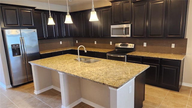 kitchen with appliances with stainless steel finishes, a sink, a center island with sink, and light stone countertops