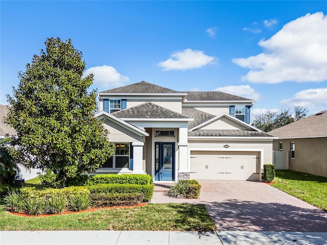 traditional-style home featuring a garage, decorative driveway, a shingled roof, and stucco siding