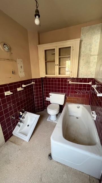 bathroom with toilet, a bathing tub, and tile walls