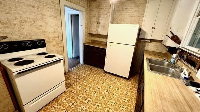 kitchen featuring white cabinetry, sink, white appliances, and brick wall