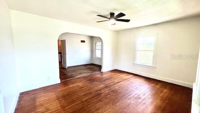 214 N New Hampshire Ave, Tavares, FL 32778 - unfurnished room featuring arched walkways, ceiling fan, dark wood-style flooring, and baseboards