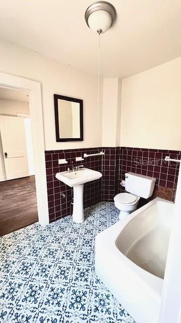 214 N New Hampshire Ave, Tavares, FL 32778 - bathroom with tile walls, toilet, wainscoting, tile patterned floors, and a tub to relax in