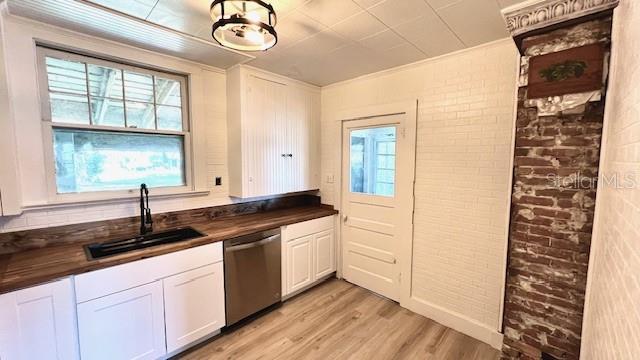 214 N New Hampshire Ave, Tavares, FL 32778 - kitchen with stainless steel dishwasher, a sink, brick wall, light wood-type flooring, and white cabinetry